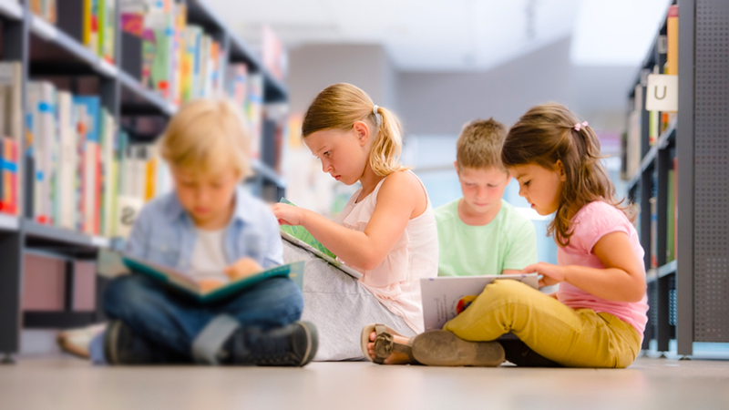 Group of children sitting on floor an reading books in the public library.