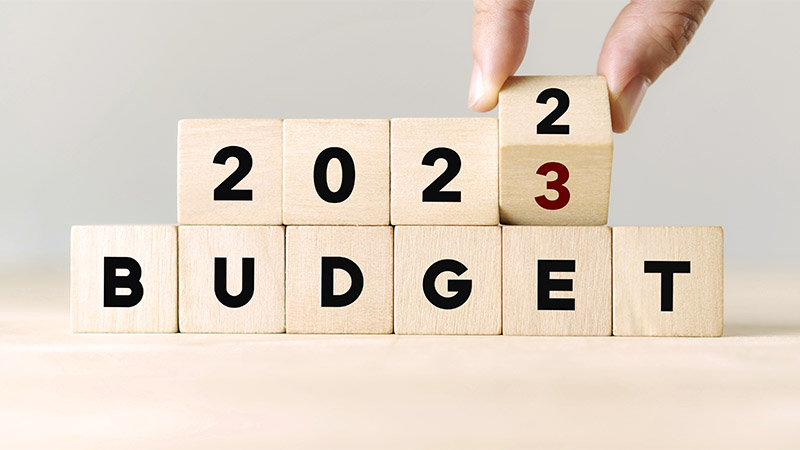 2023 Budget planning. Hand flips wooden cube and changes the inscription "BUDGET 2022" to "BUDGET 2023" with grey background, copy space.