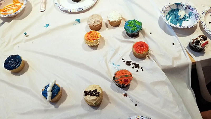 Several cupcakes on a table covered with a sheet in the process of being decorated
