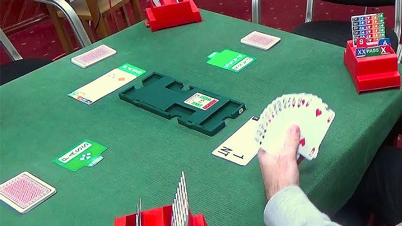 A table covered with green felt and a bridge system with a hand of cards