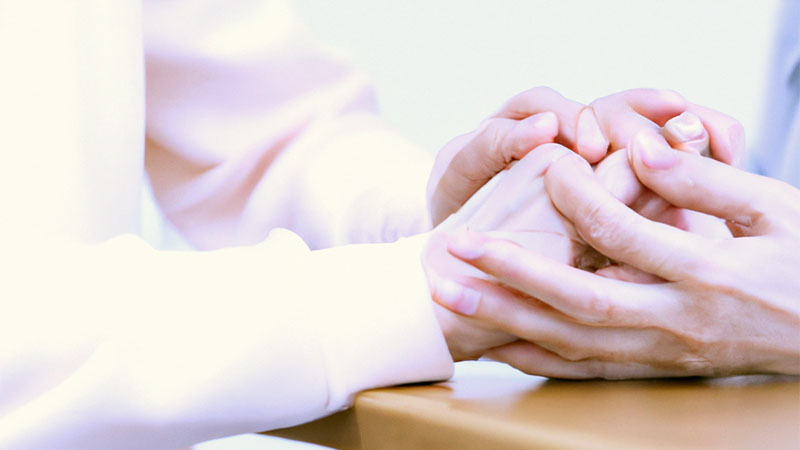 Caregiver helping an elderly person sitting a table by holding their hands.