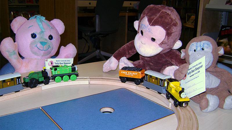 Teddy Bears sitting around a wooden train track waiting for a story.