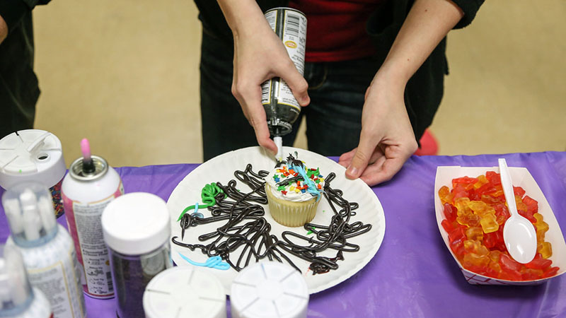 Photo of a cupcake wars participant putting whipped cream on a cupcake sitting on a paper plate.